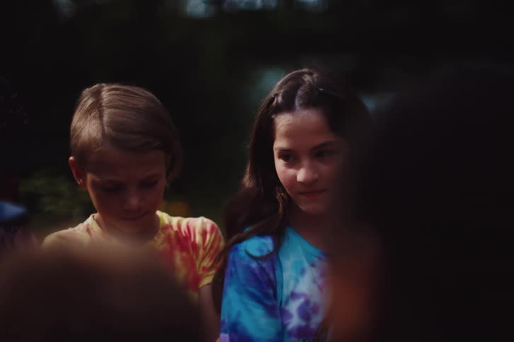 A group of children attentively gathered outdoors with two girls in colorful tiedye shirts standing out