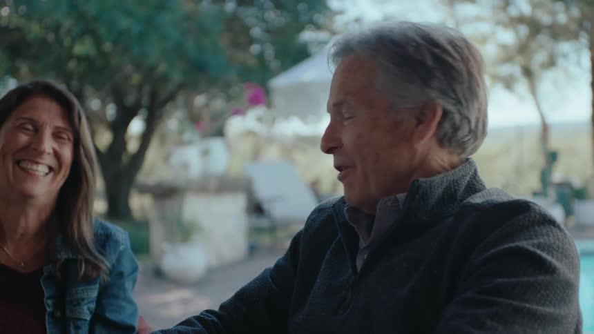 Older man and woman smile while having a conversation on a patio