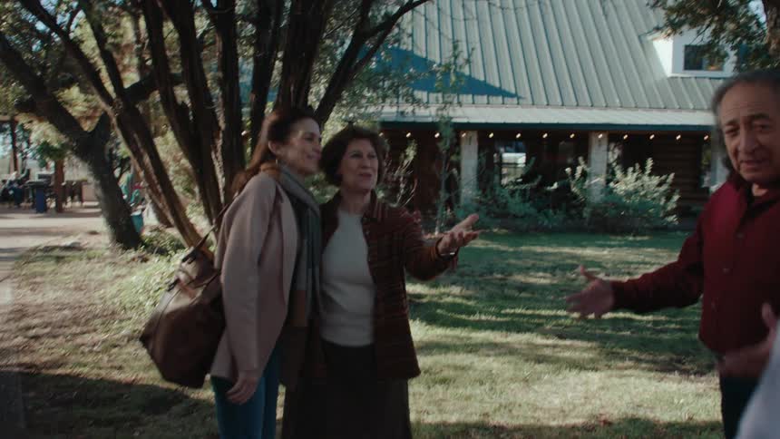A grayhaired man with a suitcase in his hand hugging another man and then greeting two women who are holding each others hands