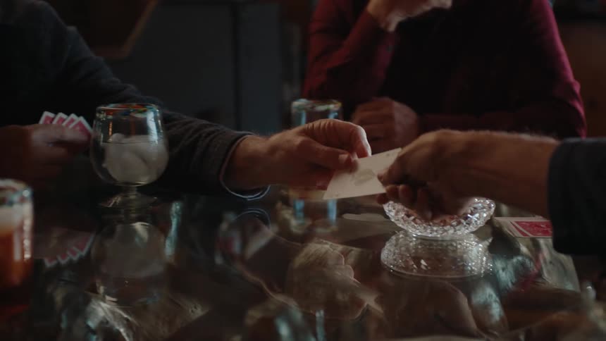 Group of people sitting at a glass table playing cards