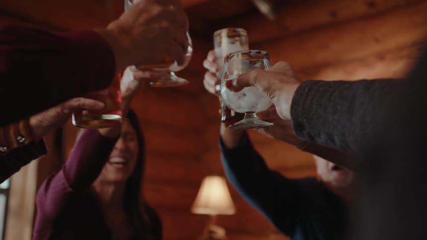 A group of people sit around a table raising their glasses in a toast in a cozy wooden interior