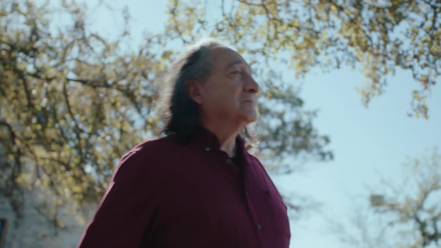 Elderly man walking through a yard with trees