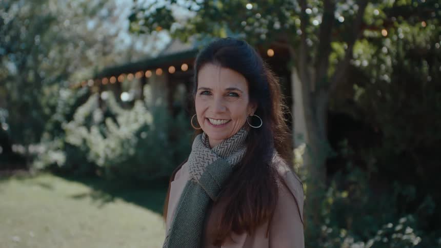 Woman dressed for cool weather smiles while standing in the yard of a house