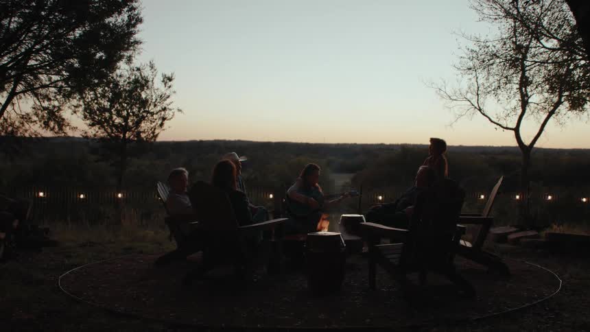 A group of people talking and singing around a campfire