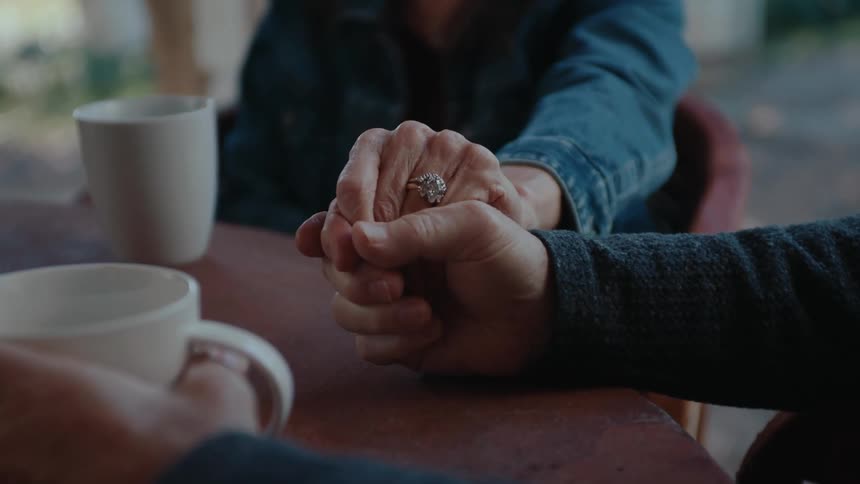 Elderly couple holding hands together while sitting at a table