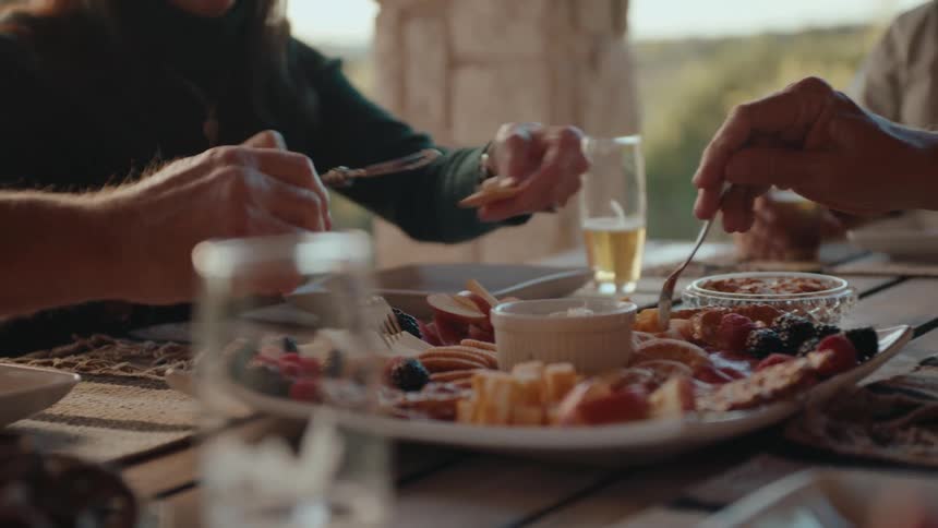 A closeup of a charcuterie board with a variety of food and people reaching for it