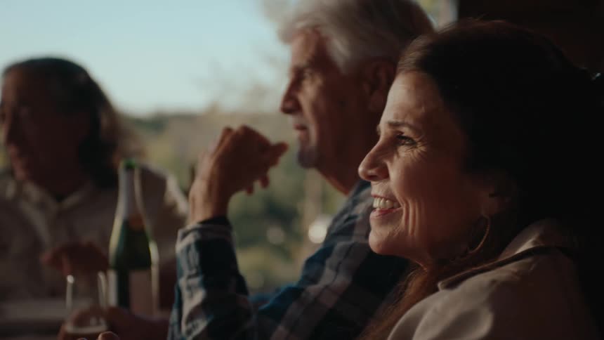 A man and a woman talk and laugh while sitting at a table on a patio and having some wine