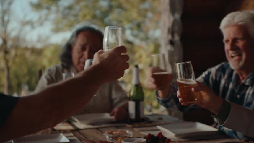 A group of people sitting together outdoors clinking glasses in a toast