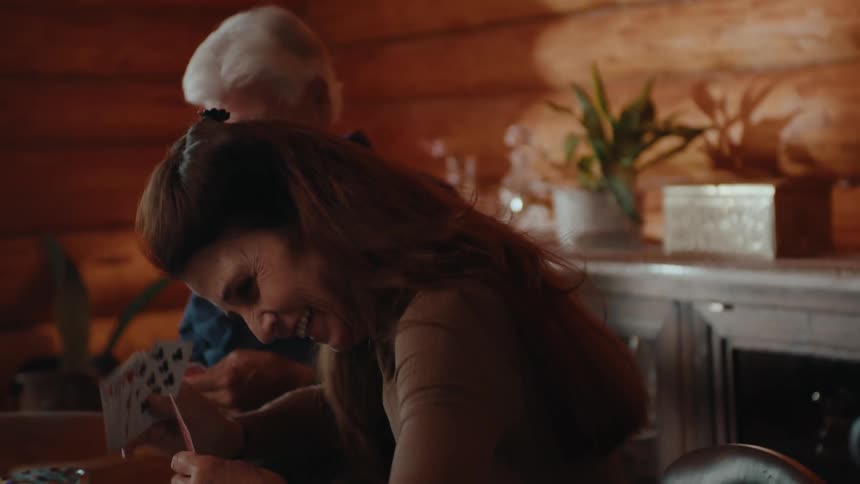 A woman and a man are playing cards laughing and enjoying themselves in a log cabin