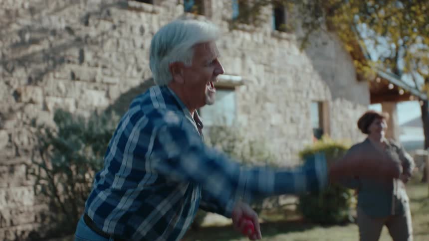 Elderly man in backyard throwing objects and cheering happily while playing