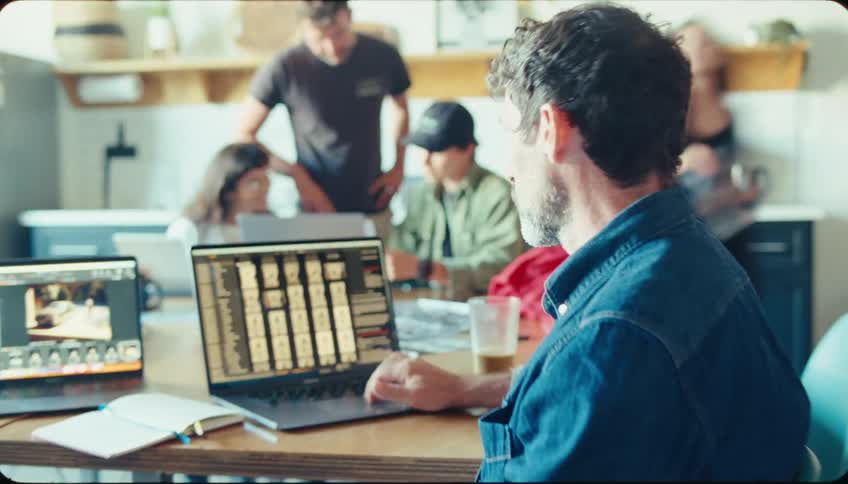 A man looks at a laptop and looks suddenly frightened as people talk together in the background