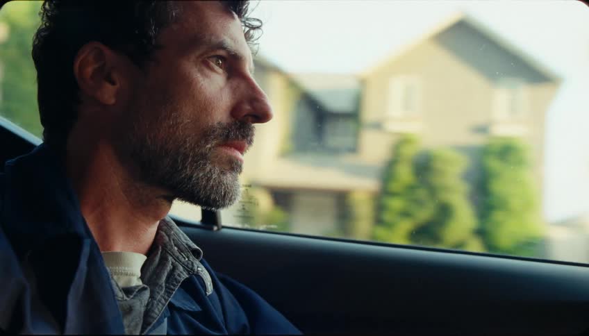A man thinks as he rides in a car through a suburb