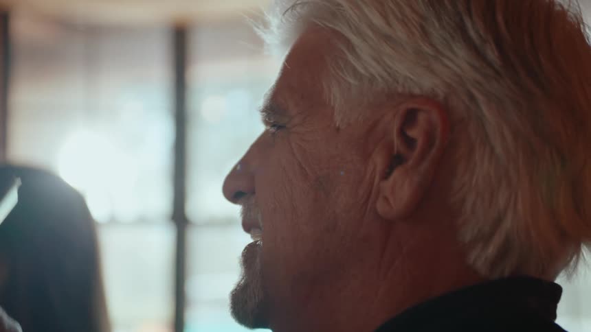 The face of a gray-haired man who is smiling while holding some cards from a deck