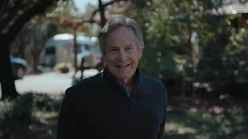 A person stands outdoors in a garden with trees and vegetation in the background