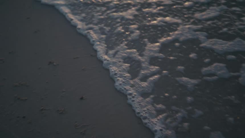 A foamy tide washes into a beach at sunset