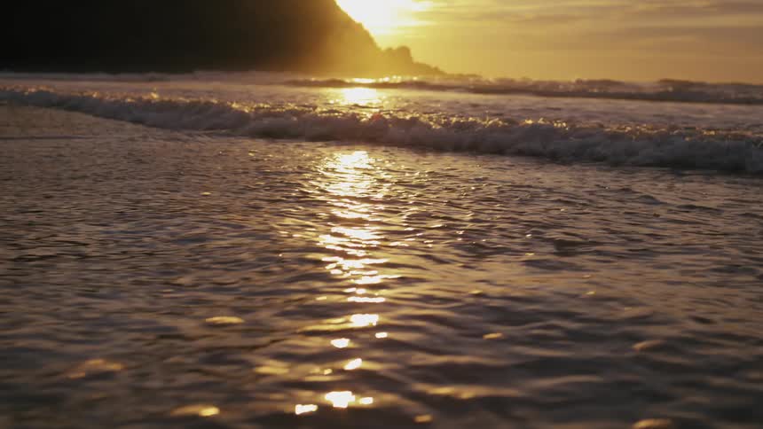 Some little waves breaking on a shallow beach with strong sunlight reflecting on the water surface in the morning