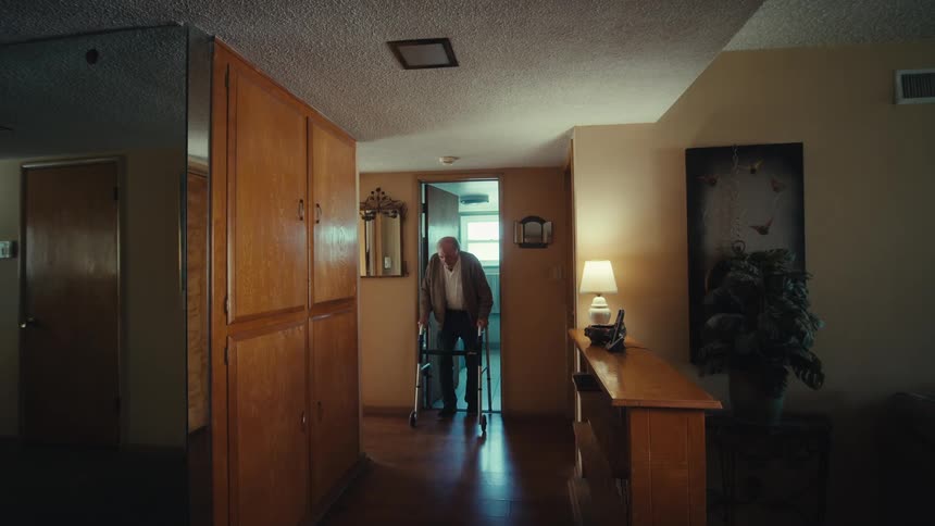 Elderly man with the help of a walker leaving the bathroom and walking down the hallway of the house