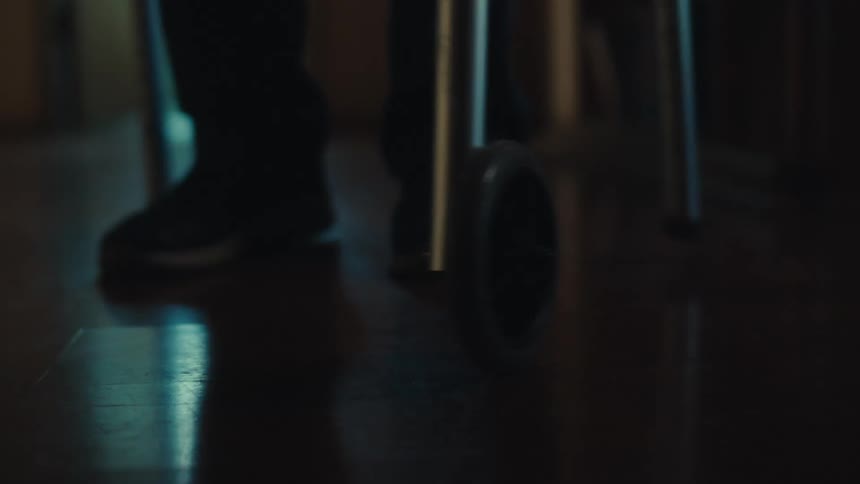 Closeup of a persons feet walking with the help of a walker down a hallway in a house