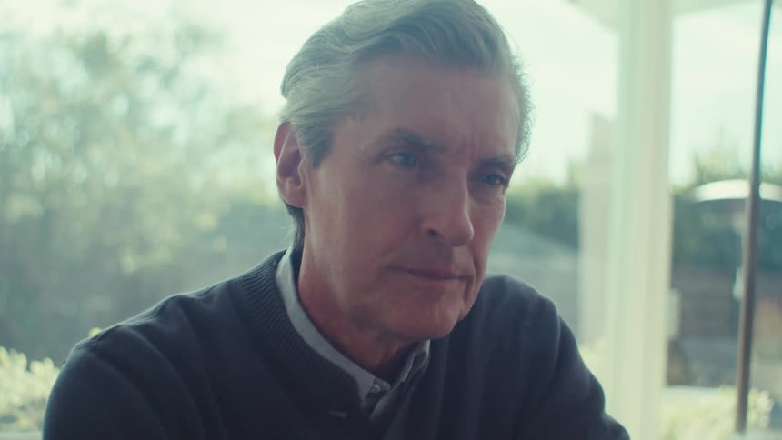 Older man sits on a couch viewing a device screen
