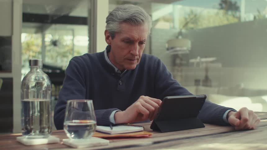 Man makes a note while viewing a tablet screen at home