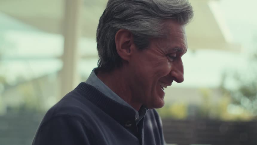 A gray haired man is talking to someone in front of him and he is smiling while talking