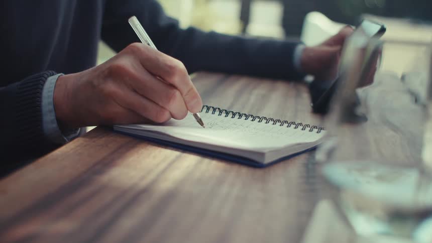 A man writes notes while looking at his tablet
