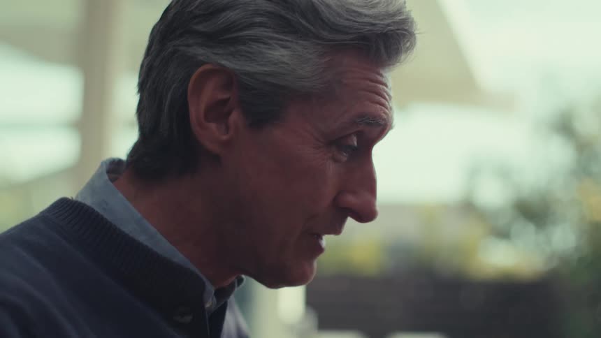 Older man smiles while sitting at a table during a video call