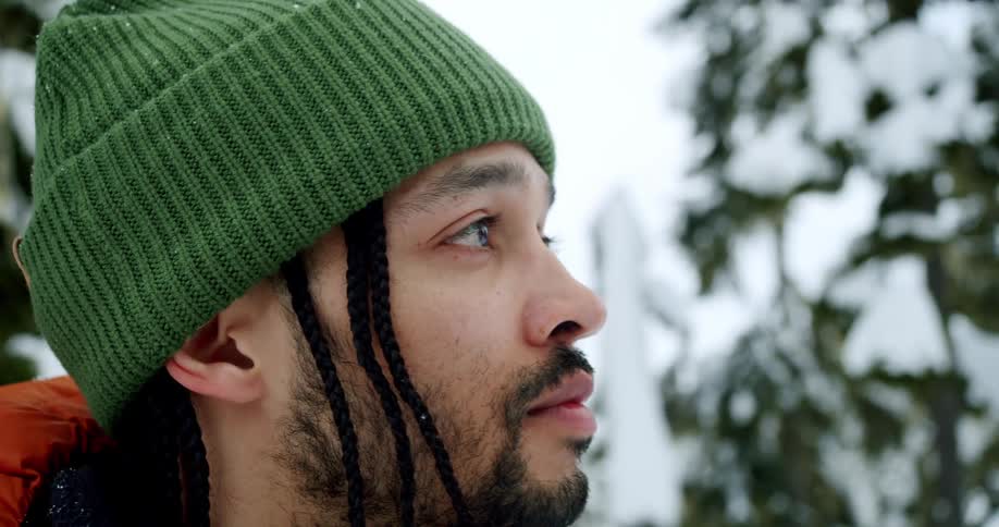 Male hiker stands outdoors in a forest while it snows