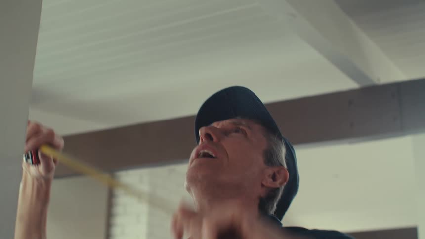 Man in cap with tape measure measuring ceiling