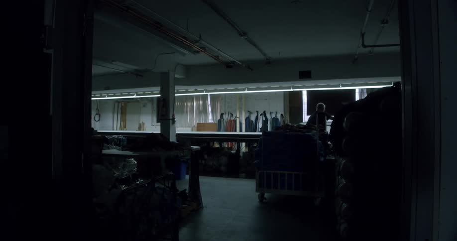 A worker is unrolling a large piece of cloth on a table in a dimly lit workshop