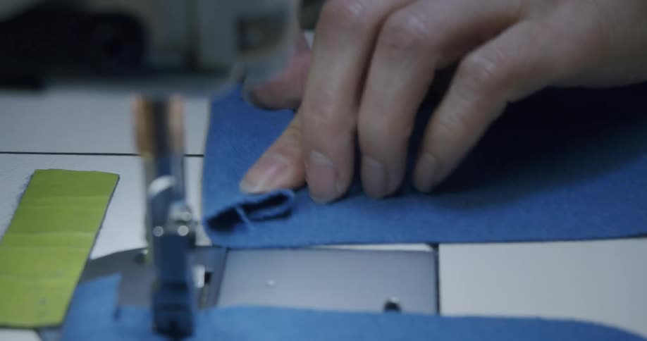 Hand handling blue fabric towards a sewing machine