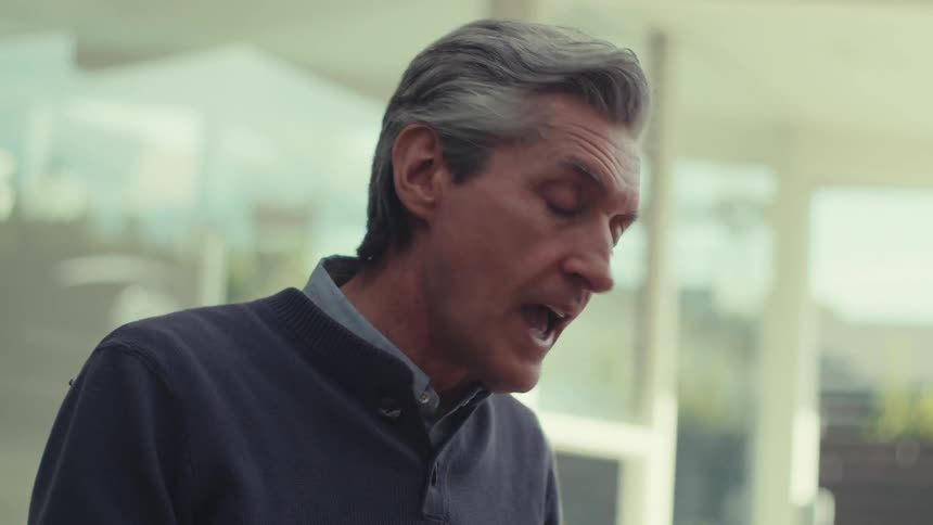 A person with gray hair wearing a dark jacket is standing outdoors having a conversation