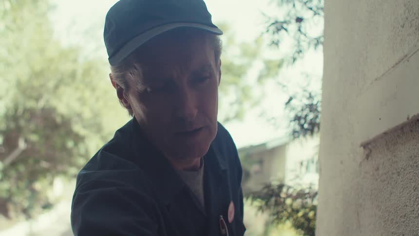 Working service white man standing outdoors during daytime on a suburban area measuring an area of a wall with a measuring tape