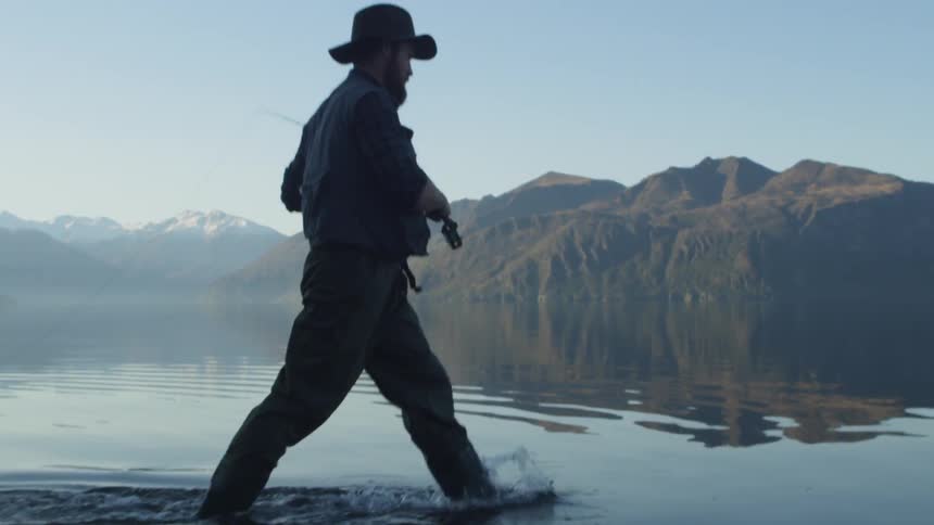 A fisherman wades near the shore and casts his line in a calm lake