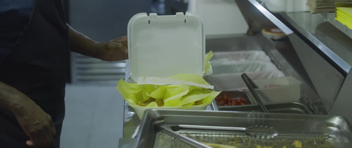 A persons hands are shown preparing food orders in a restaurant kitchen