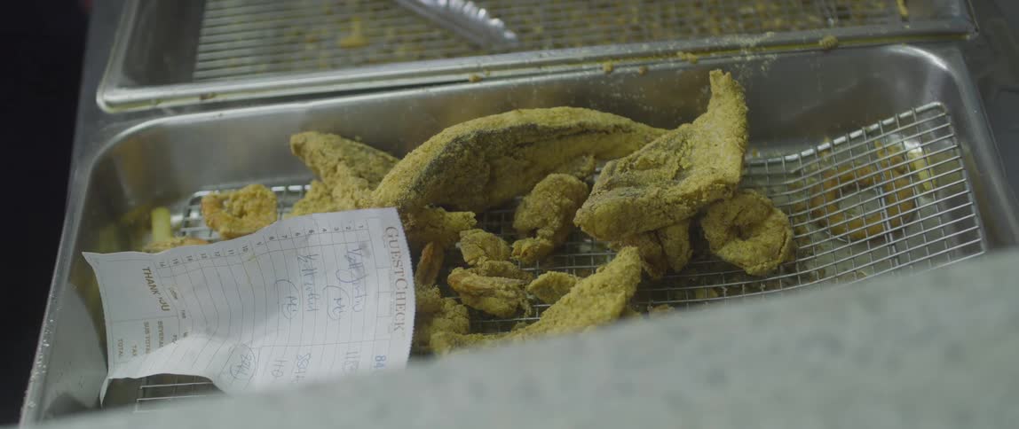 Fried fish and other food items sit on a metal grate with a customer receipt visible
