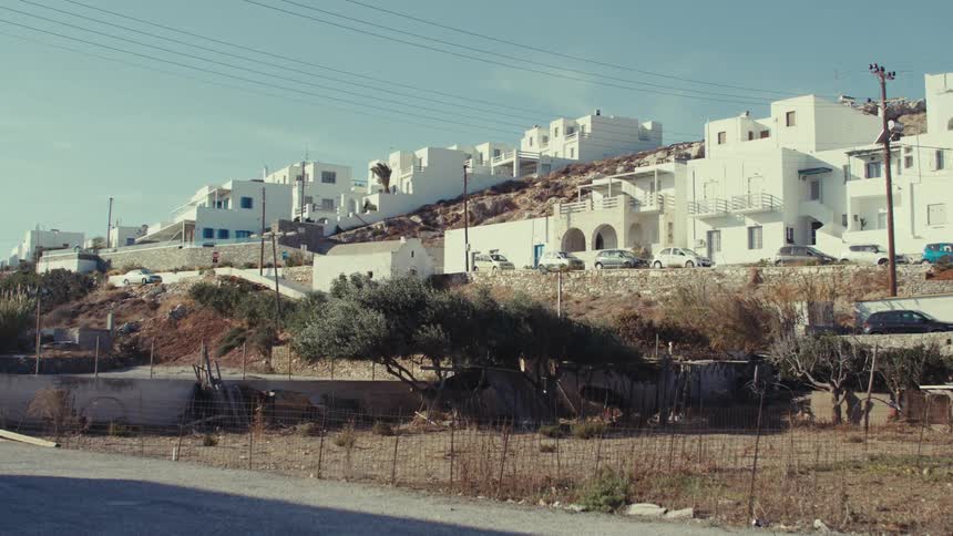 A cluster of whitewashed buildings clings to a sunbaked hillside overlooking a barren landscape