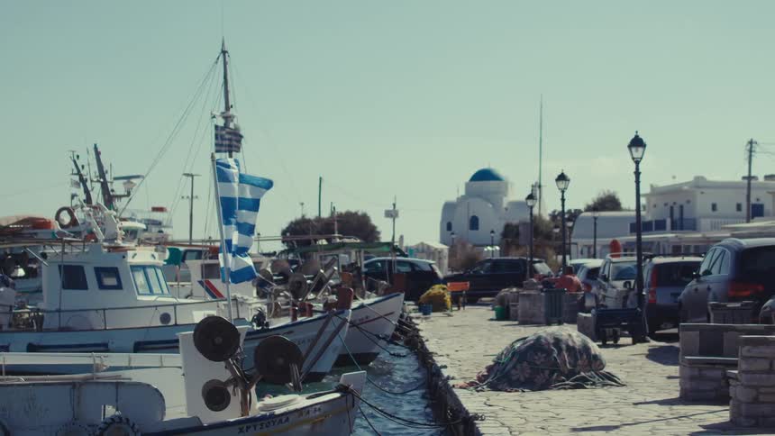 A peaceful harbor scene in greece with whitewashed buildings blue domes and traditional fishing boats under a clear sky