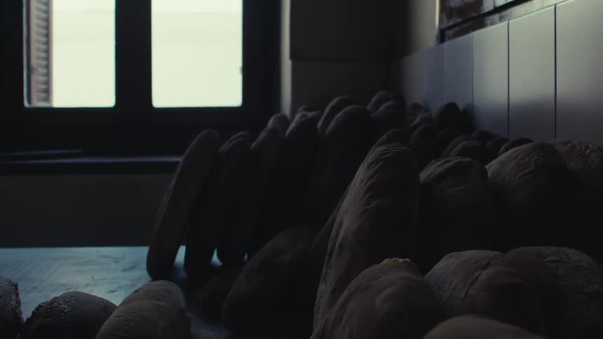 Loaves of bread stacked in a dimly lit bakery room