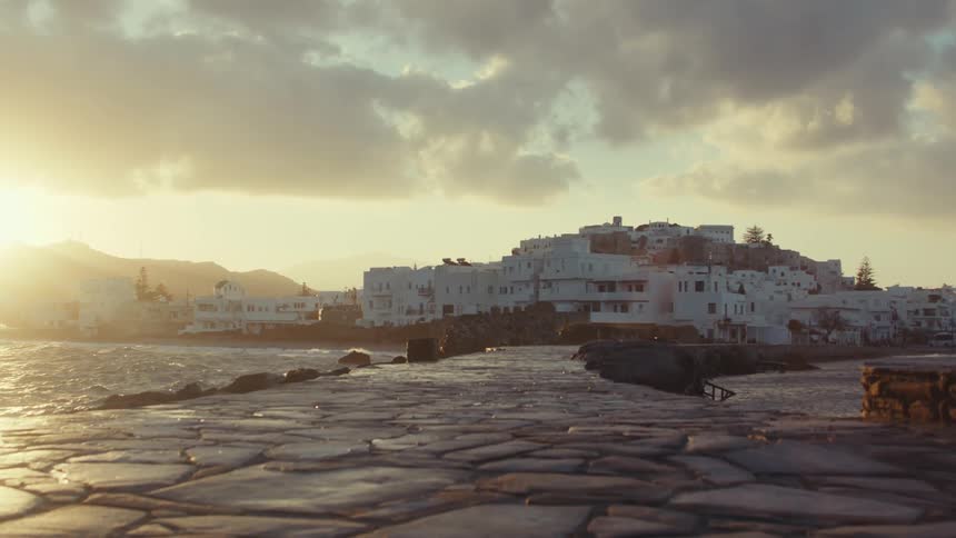 Densely packed houses with a flagstone path meet the ocean at sunset