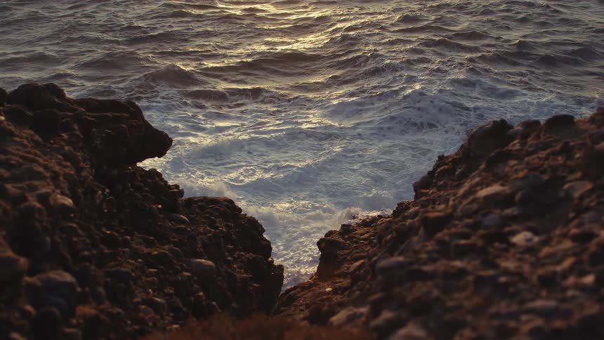Ocean waves crash against sharp rocks at the coast