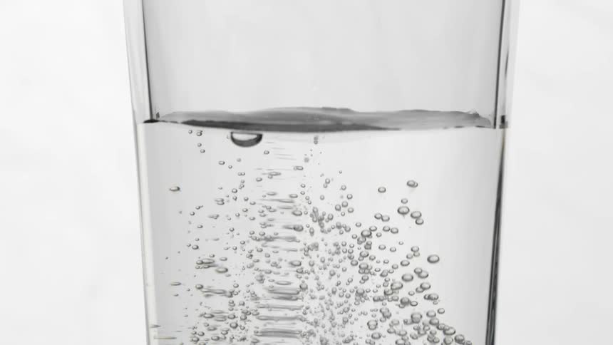 An effervescent antacid tablet drops into a glass of water