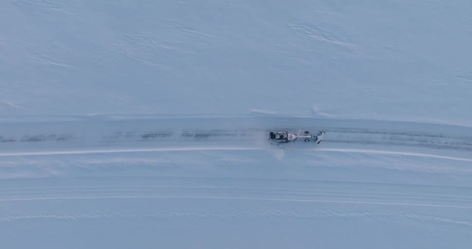 A lone snow plow carves a path through a vast untouched expanse of snow