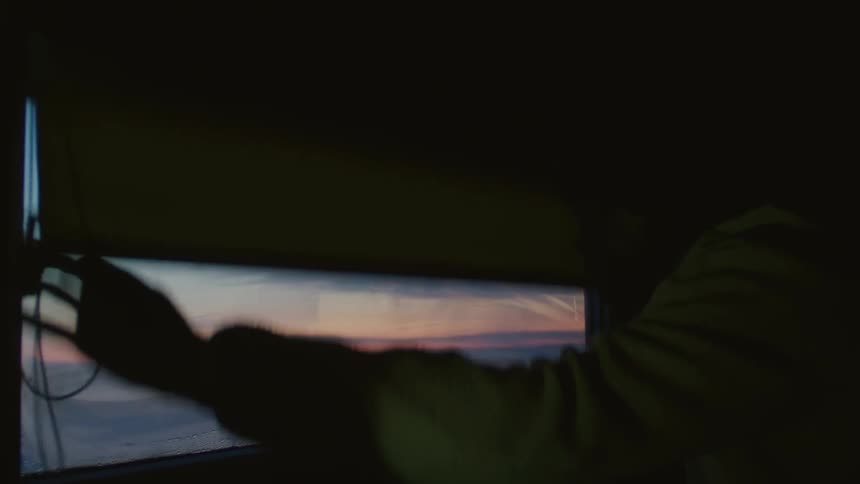 A silhouette of a person gazing at a colorful sunset through a window