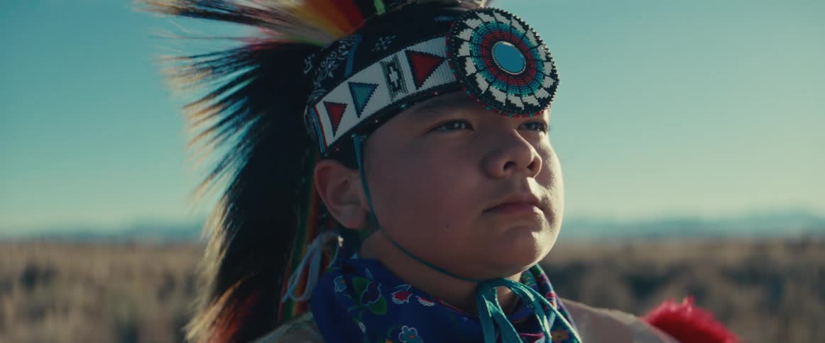 Portrait of a young man wearing native american attire with feathers while standing in a natural setting
