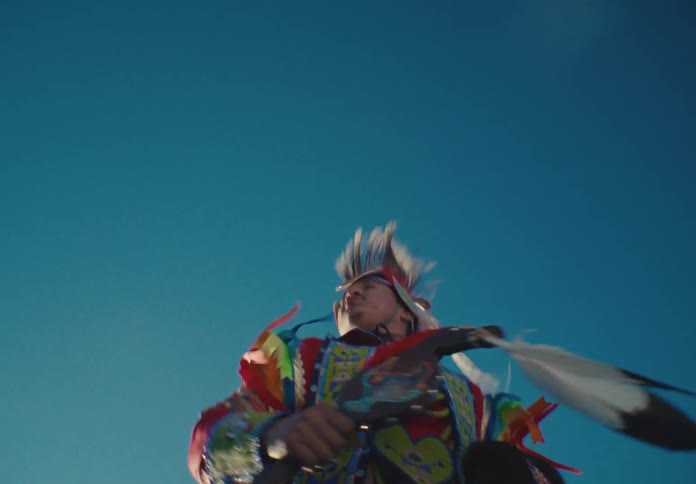 A native american dancer in vibrant regalia performing against a clear blue sky