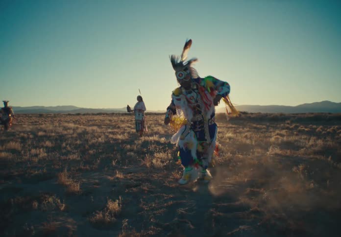 Group of people dancing in a field while wearing traditional native american attire