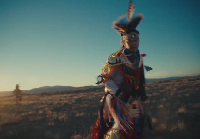 A person in colorful feather clothing performing a ritualistic dance in a desert region