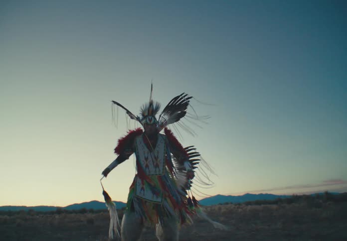 Person wearing native american costume and dancing in a field at dawn