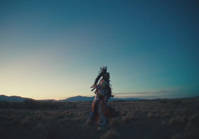 Man in traditional native american clothing dancing in a desert environment with sparse vegetation